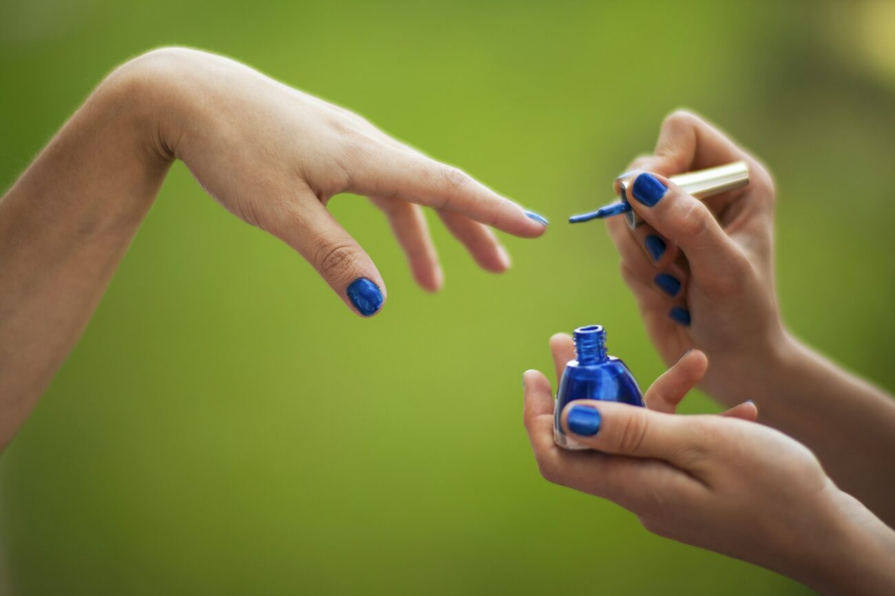 Blue nail polish being painted onto a fingernail