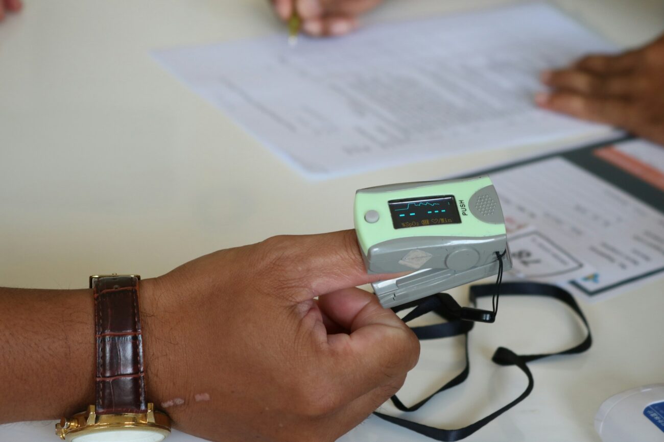 A fingertip pulse oximeter clipped on a person's finger, its display lit