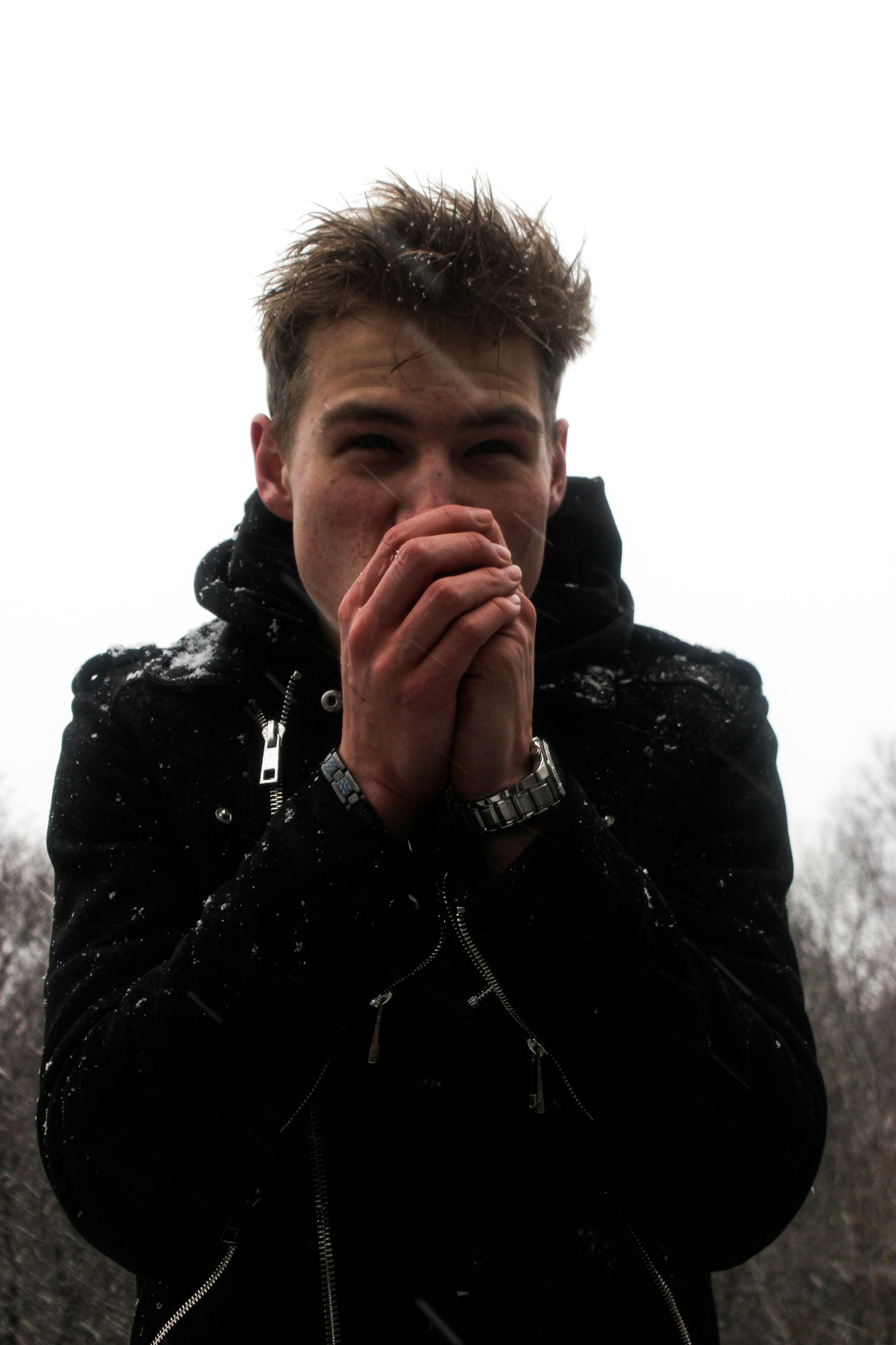 A man in a snow-dusted jacket cupping his cold hands to his mouth to warm them